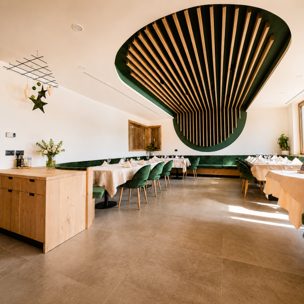 Sala ristorante moderna dell'Hotel Olimpionico con soffitto scenografico in legno e metallo, sedute verdi imbottite e arredamento alpino contemporaneo realizzato su misura da Arredamenti Depal.