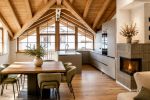 cucina e sala da pranzo su misura in mansarda alpina con travi in legno a vista, camino e ampie vetrate