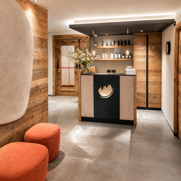 Reception di centro benessere e spa con arredi su misura in legno, banco accoglienza moderno, illuminazione d’atmosfera e dettagli dal design alpino contemporaneo.