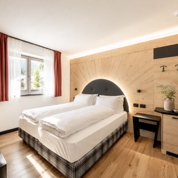 Camera d’hotel con letto matrimoniale, testata retroilluminata dal design contemporaneo, arredi su misura in legno e dettagli ispirati all’ambiente alpino.