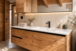 Vista dall’esterno verso l’interno di uno chalet di montagna contemporaneo. Le ampie porte finestre in legno aperte conducono a una zona pranzo e cucina su misura caratterizzata da materiali naturali, travi a vista e illuminazione calda che crea un’atmosfera accogliente.