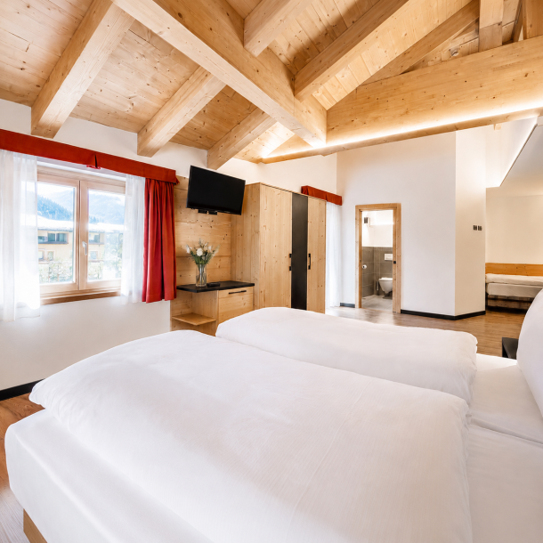 Camera d’hotel in stile alpino moderno con travi in legno a vista, arredi su misura, armadio integrato e ambienti luminosi.