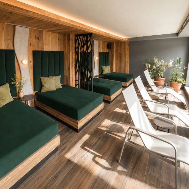 Zona relax di centro benessere con chaise longue imbottite, lettini prendisole, rivestimenti in legno e atmosfera elegante dedicata al benessere.