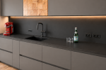 Dettaglio di cucina su misura in stile alpino contemporaneo con finiture effetto pietra, inserti in legno naturale, illuminazione LED integrata e lavello sottotop.