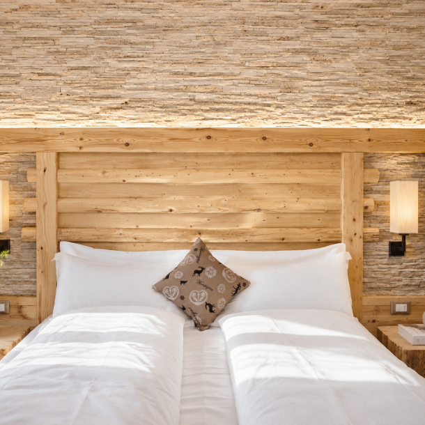 Camera dell'Hotel Plaza con testiera in legno massiccio, parete decorativa in pietra naturale e arredi alpini su misura realizzati da Arredamenti Depal.