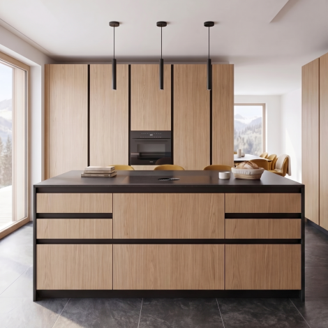 Cucina moderna su misura con grande isola centrale, finiture in rovere naturale, dettagli neri a contrasto e illuminazione minimale a sospensione. Design essenziale e contemporaneo con ampie superfici di lavoro e vista sulle montagne.